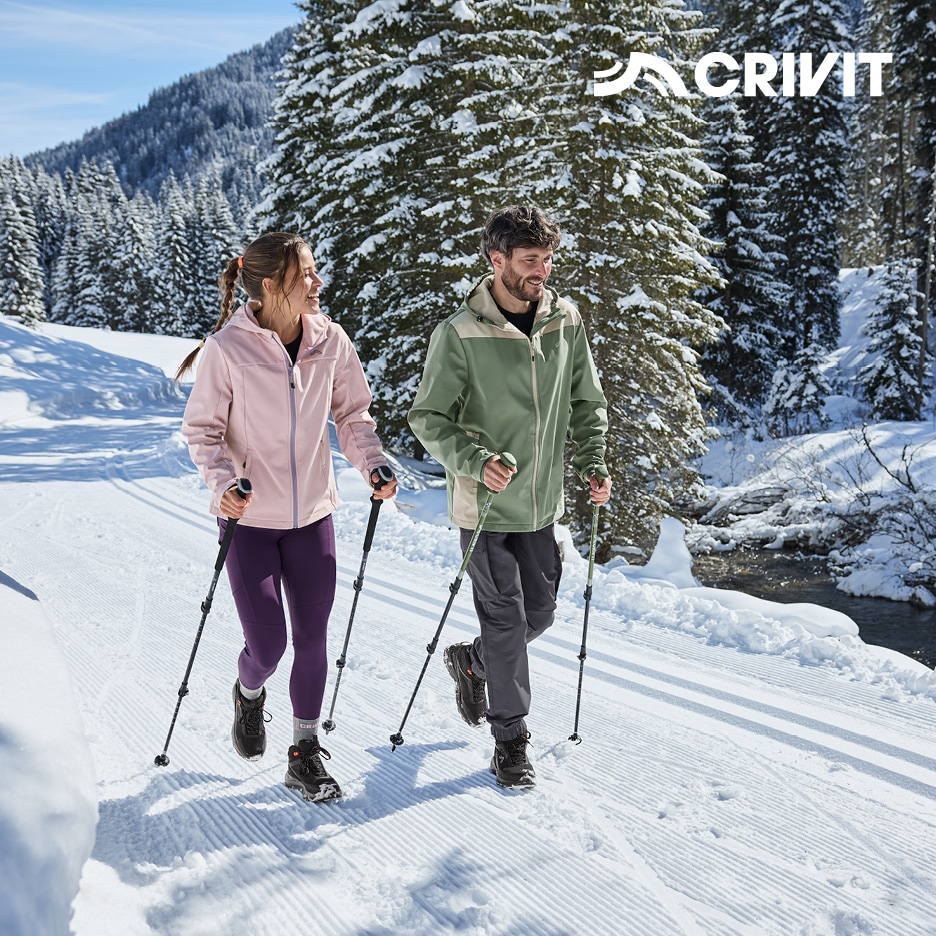 Muž a žena v outdoorovém oblečení na zimní procházce se sportovními holemi.