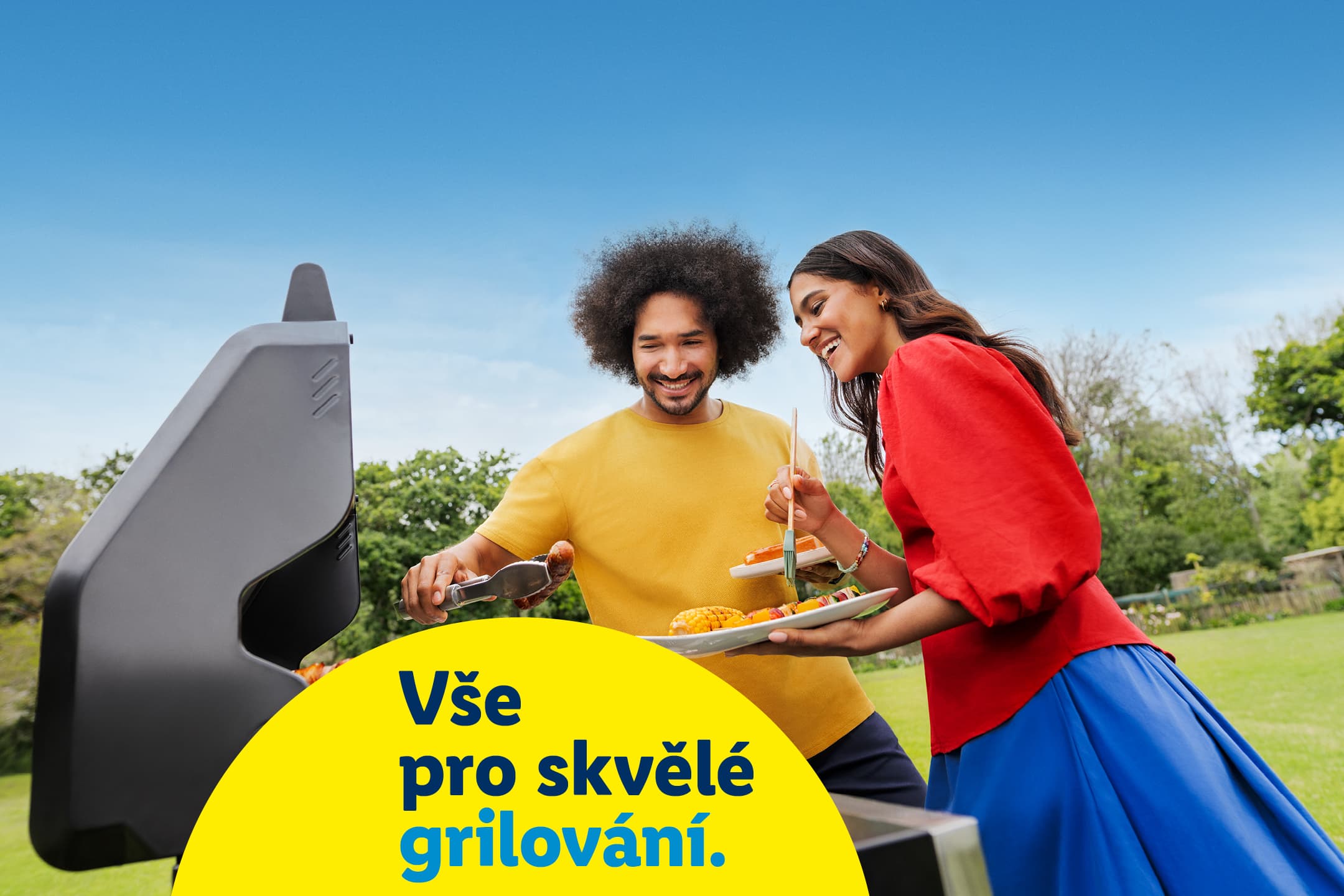 Pár griluje venku, muž obrací klobásu, žena drží talíř s kukuřicí a špízy. Text: Vše pro skvělé grilování.