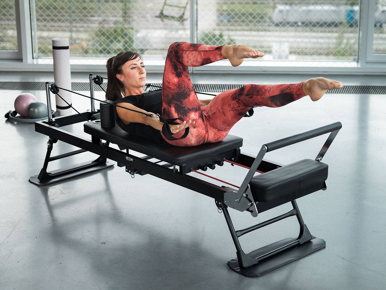 Žena cvičící Pilates na černém Pilates stroji s červenými detaily.