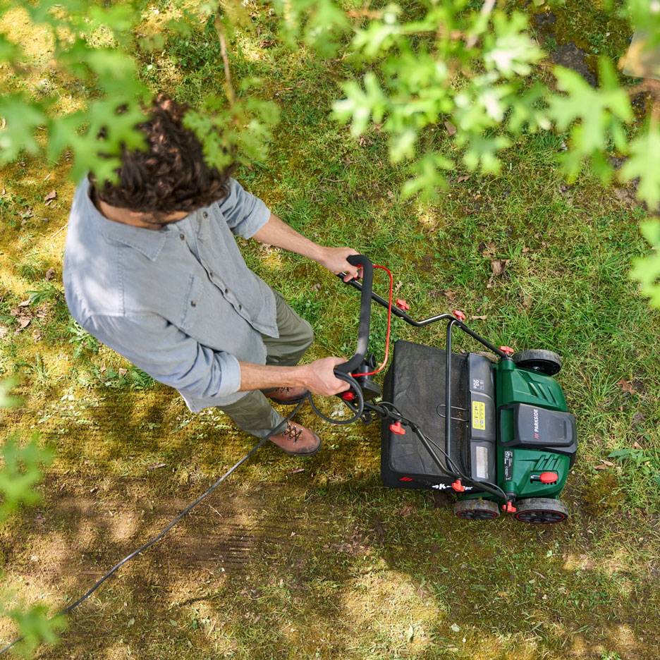 Muž seká trávník elektrickou sekačkou, pohled shora.