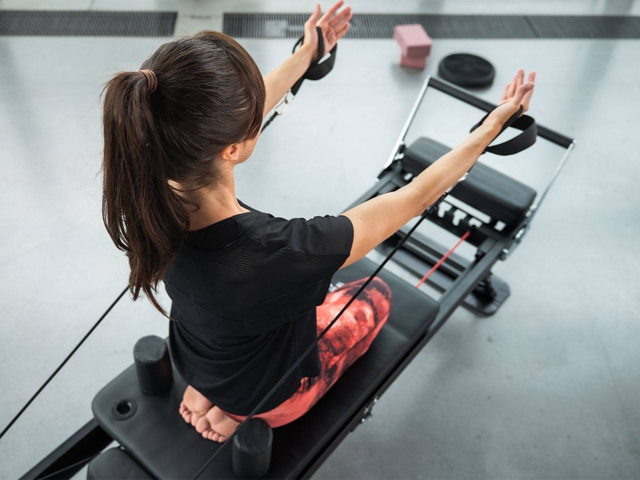 Žena cvičí Pilates na reformer stroji s odporovými pásy.