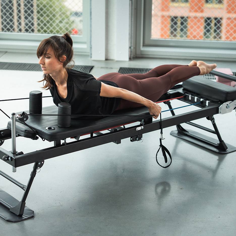 Žena cvičí na Pilates stroji s odporovými pásy.