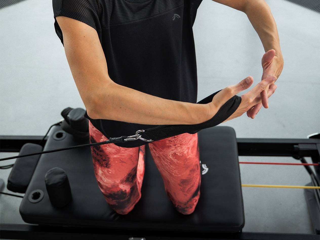 Žena cvičící s odporovými pásy na Pilates stroji.