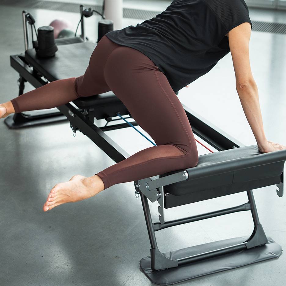 Žena cvičící na Pilates stroji, zaměřující se na nohy a hýždě.