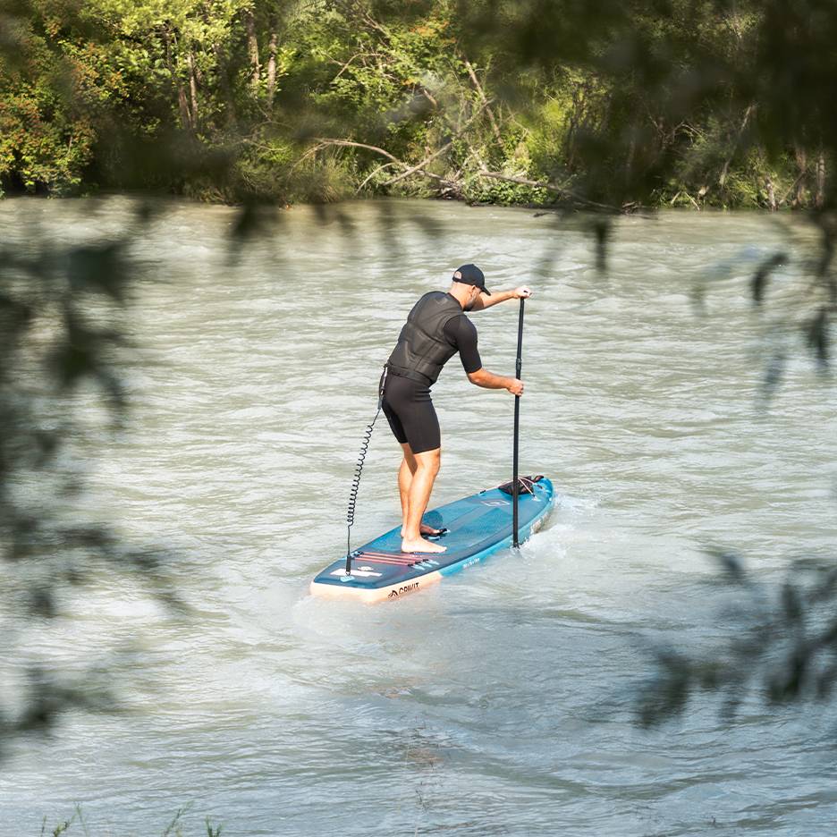Muž v neoprenu a záchranné vestě pádluje na modrém paddleboardu na řece.