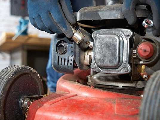 Rukavice vyměňují zapalovací svíčku na červené sekačce.