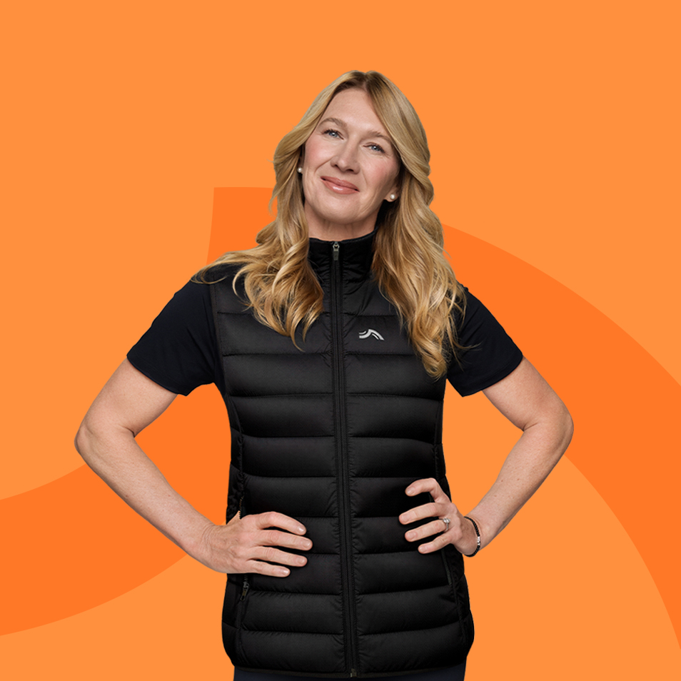 Žena v černé prošívané vestě a černém tričku, usmívající se, na oranžovém pozadí.