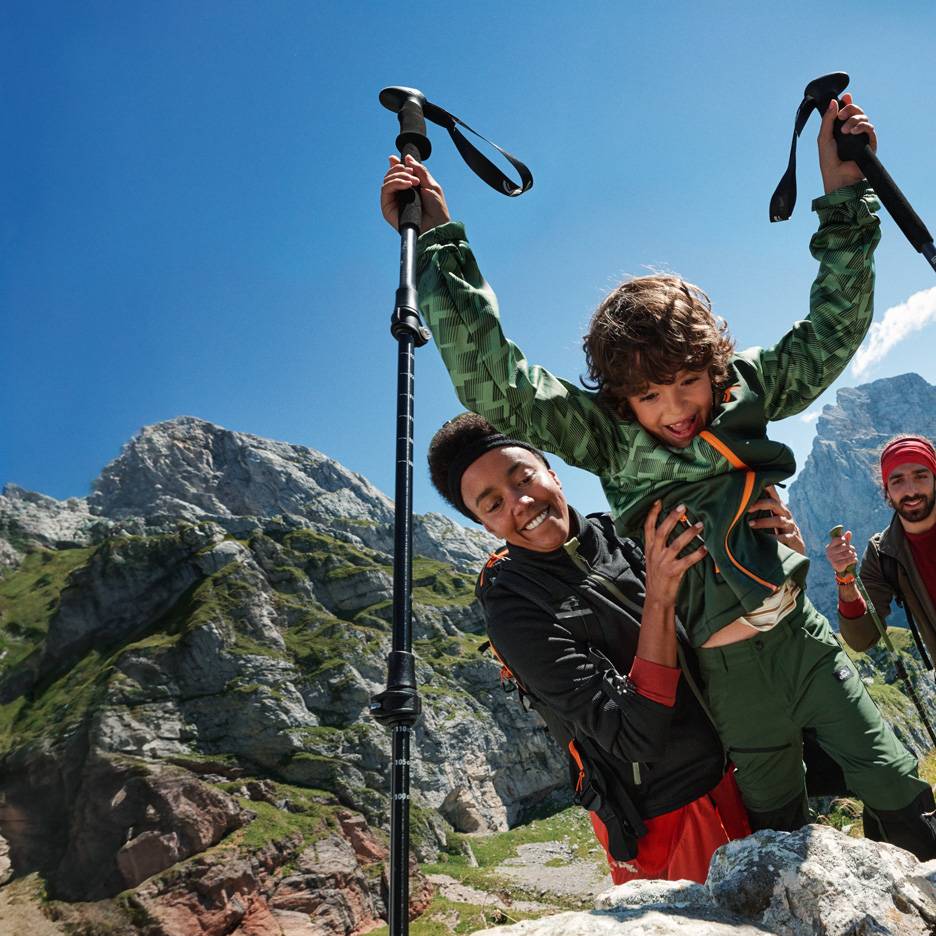 Rodina na túře s trekingovými holemi a outdoorovým oblečením v horách.