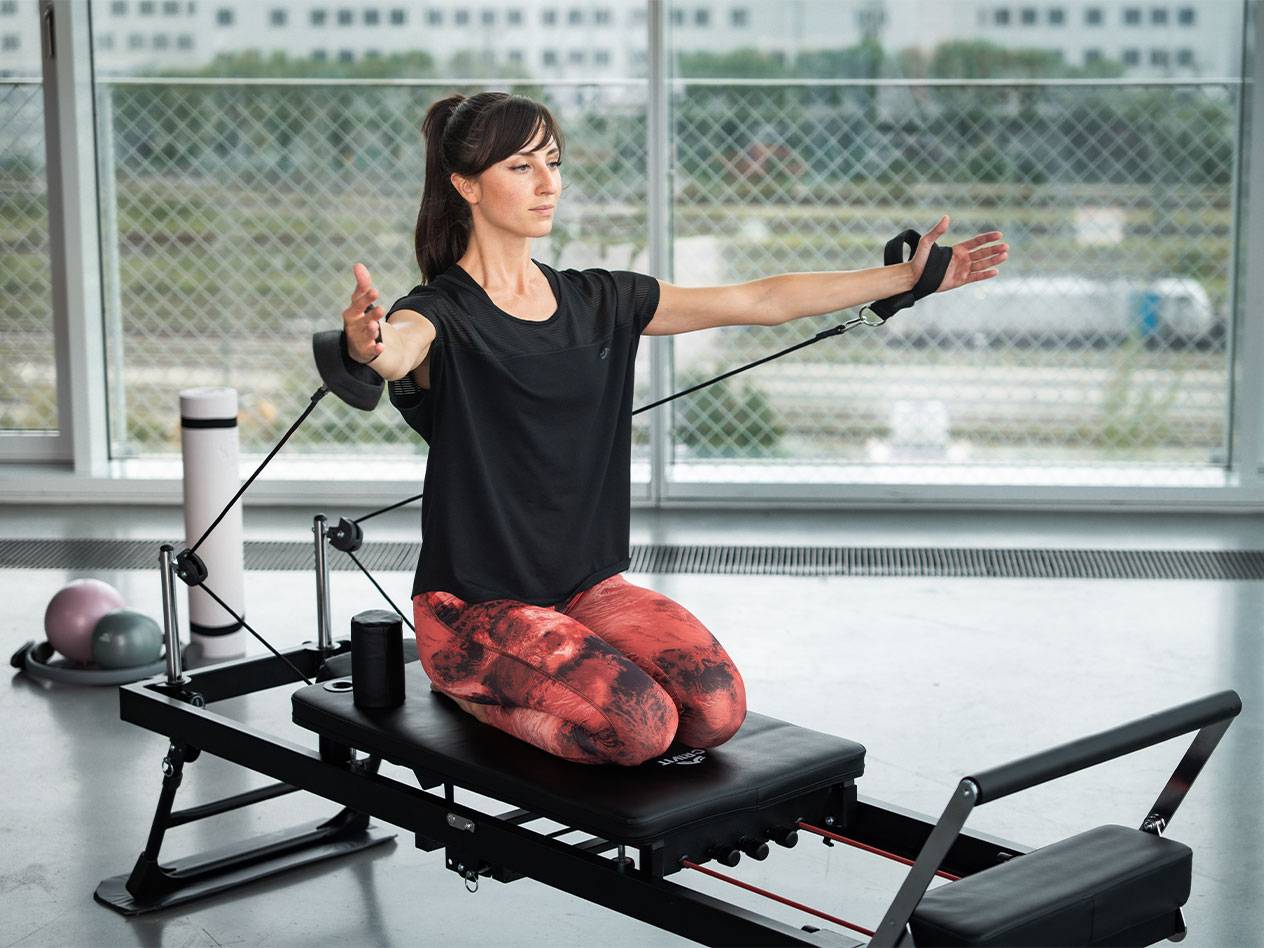Žena cvičí Pilates na reformer stroji s odporovými pásy.