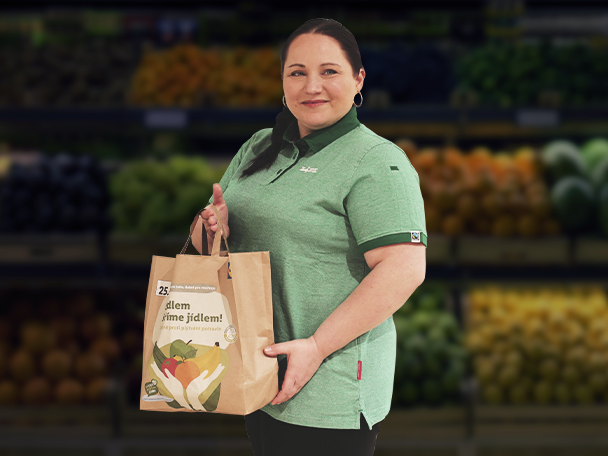 Žena drží nákupní tašku s ovocem a zeleninou v supermarketu.