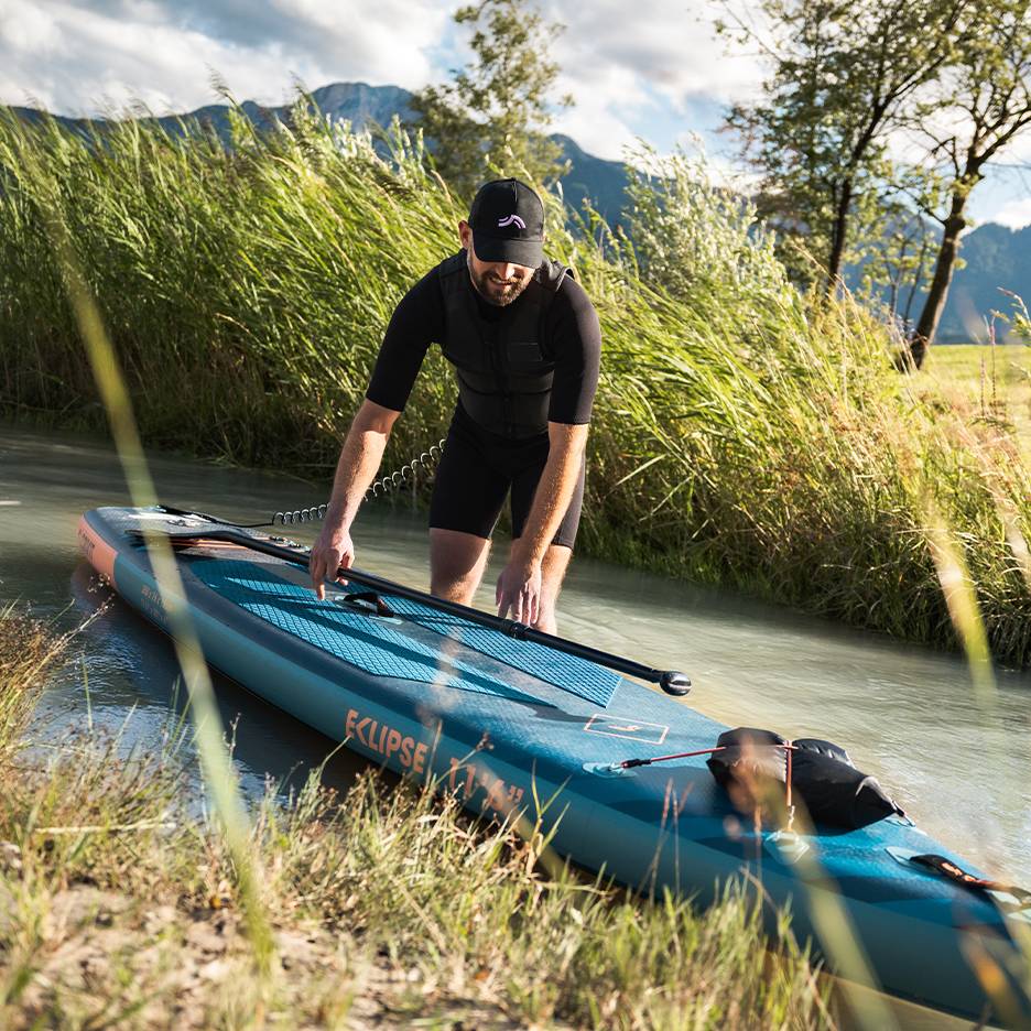 Muž v černém neoprenu se připravuje na paddleboard, prkno ve vodě