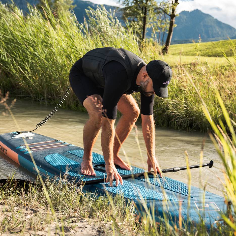 Muž v neoprenu a záchranné vestě se připravuje na paddleboarding na řece.