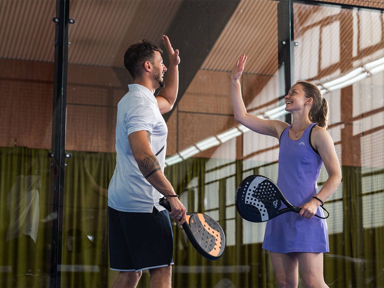 Dva hráči padelu, muž a žena, si dávají high-five na kurtu.