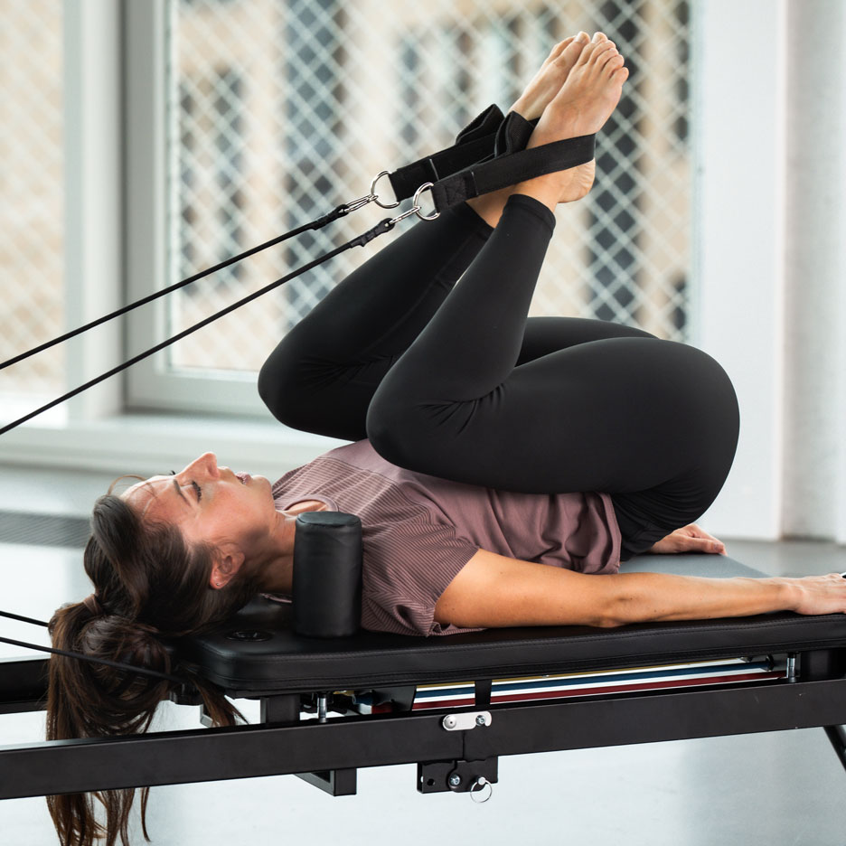 Žena cvičící Pilates na reformer stroji s nohama v popruzích.