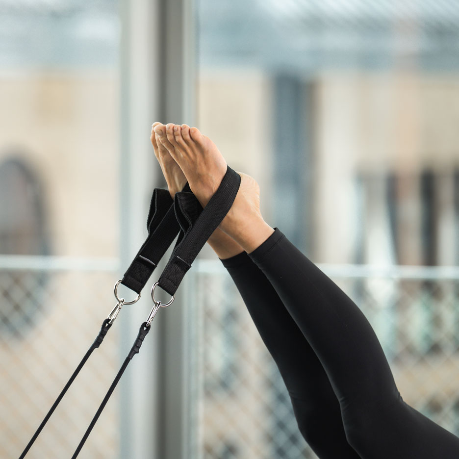 Osoba cvičící Pilates s nohama v popruzích.