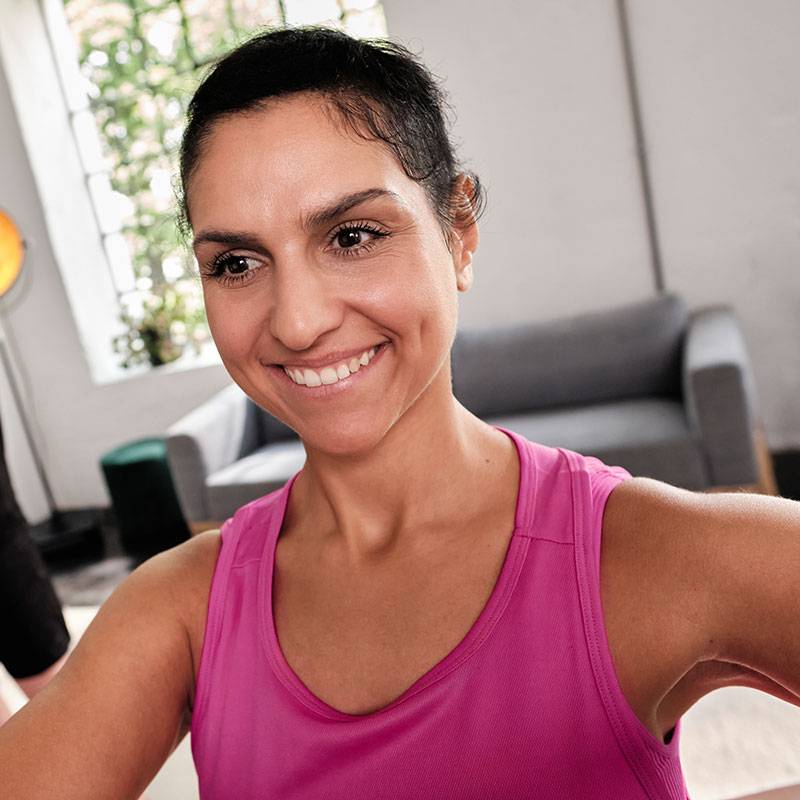 Usměvavá žena v růžovém tílku cvičí doma.