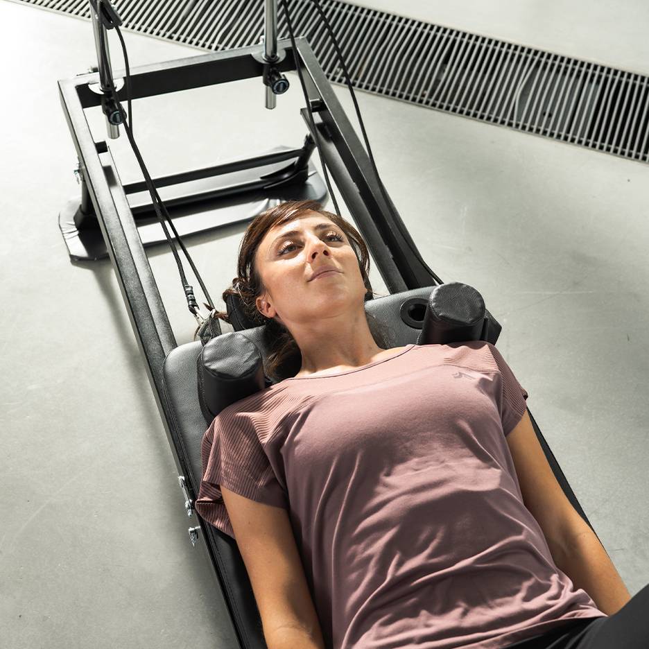 Žena ležící na fitness stroji, dívající se nahoru.