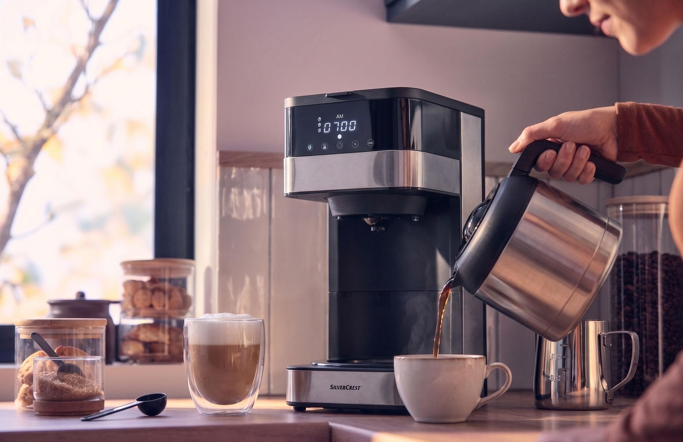 Kávovar nalévá kávu do šálku, s latté a sušenkami na pultu.