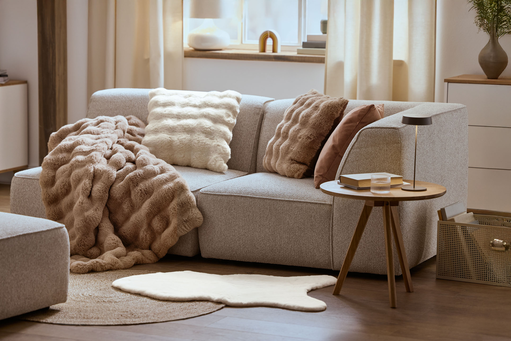 Útulný obývací pokoj s šedou pohovkou, nadýchanými polštáři a dekou, dřevěným konferenčním stolkem.