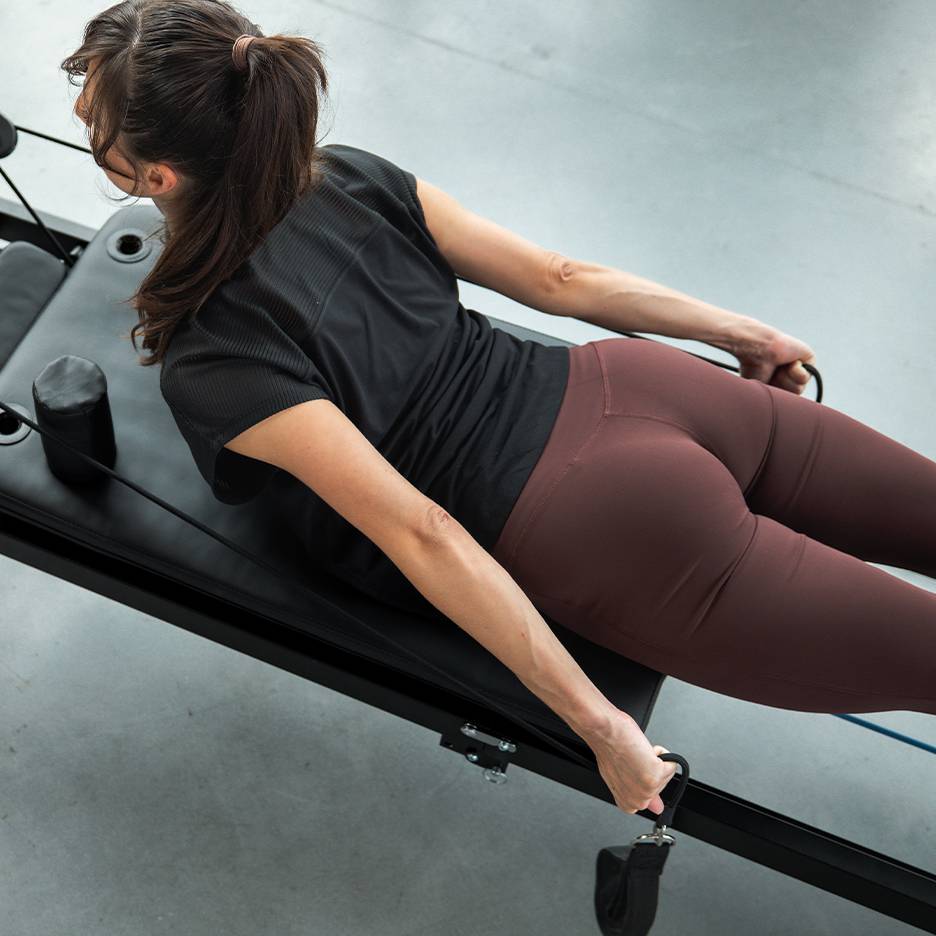 Žena cvičící na Pilates stroji s odporovými pásy, v aktivním oblečení.