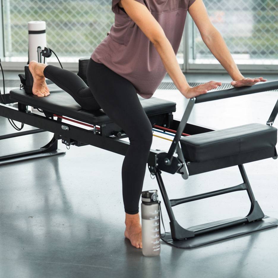 Žena cvičící na Pilates stroji s lahví vody poblíž.