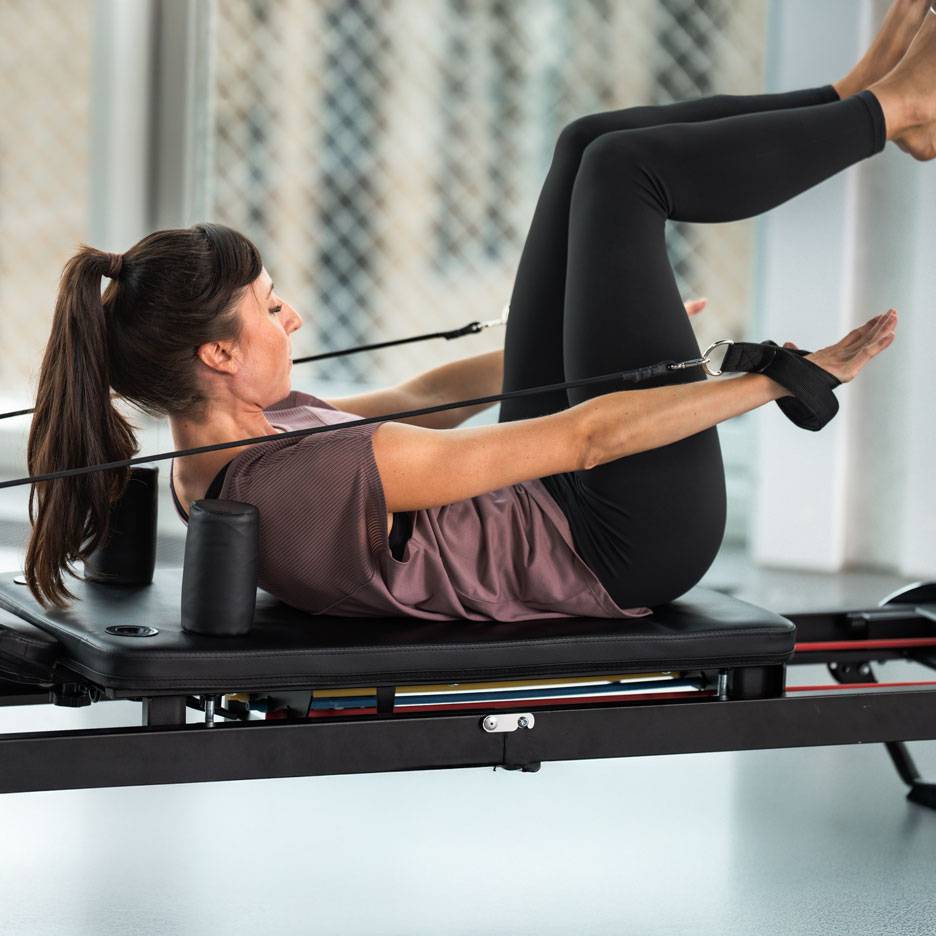 Žena cvičící Pilates na reformer stroji, v černém sportovním oblečení.
