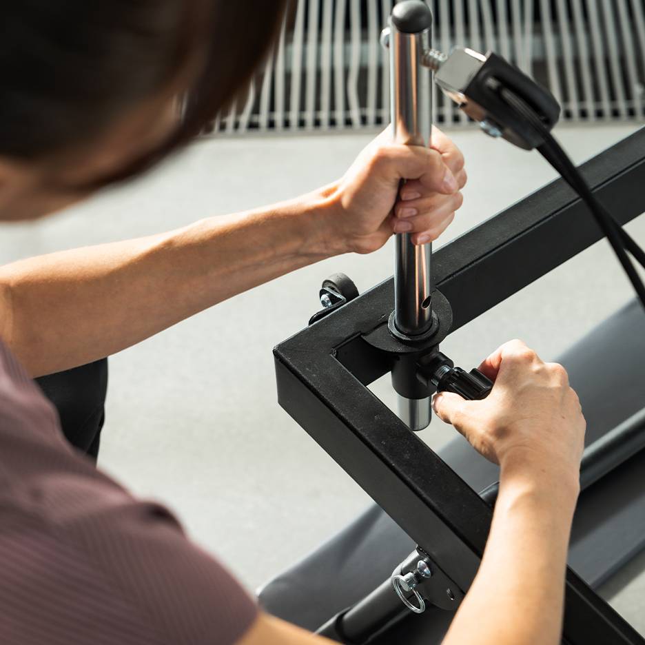 Osoba nastavující fitness vybavení, zaměřená na ruce a kovové části.