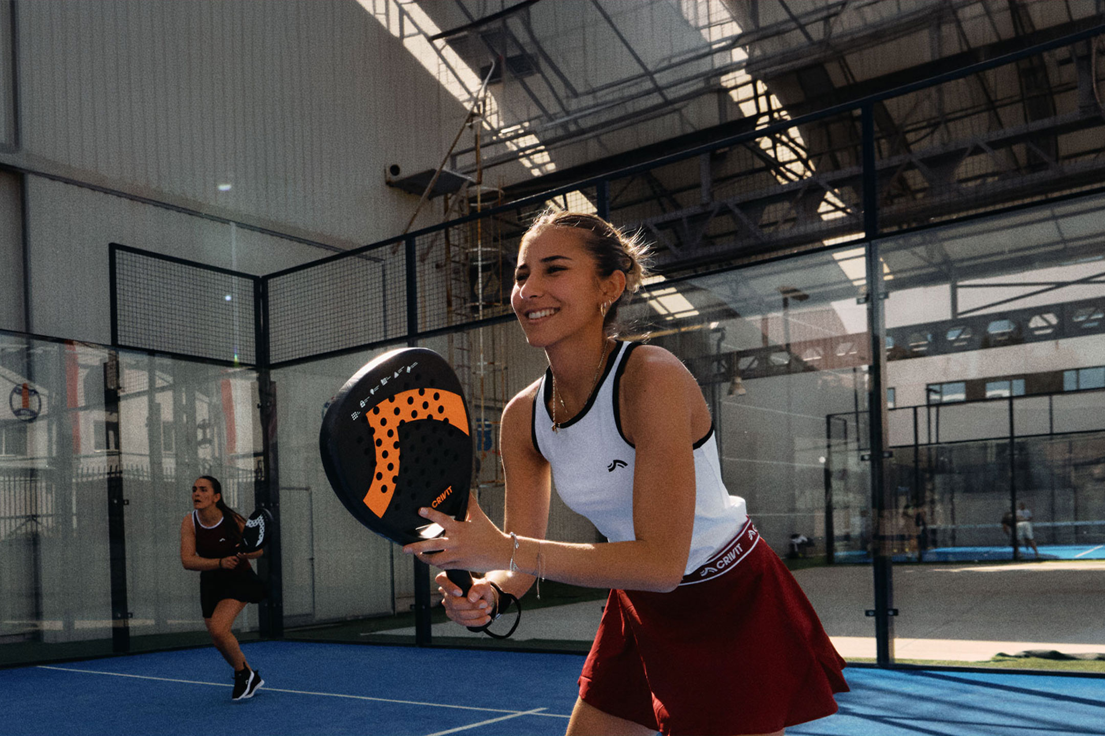 Obrázek vytvořený AI: Dvě ženy hrající padel tenis, jedna se usmívá a drží raketu, na modrém kurtu.