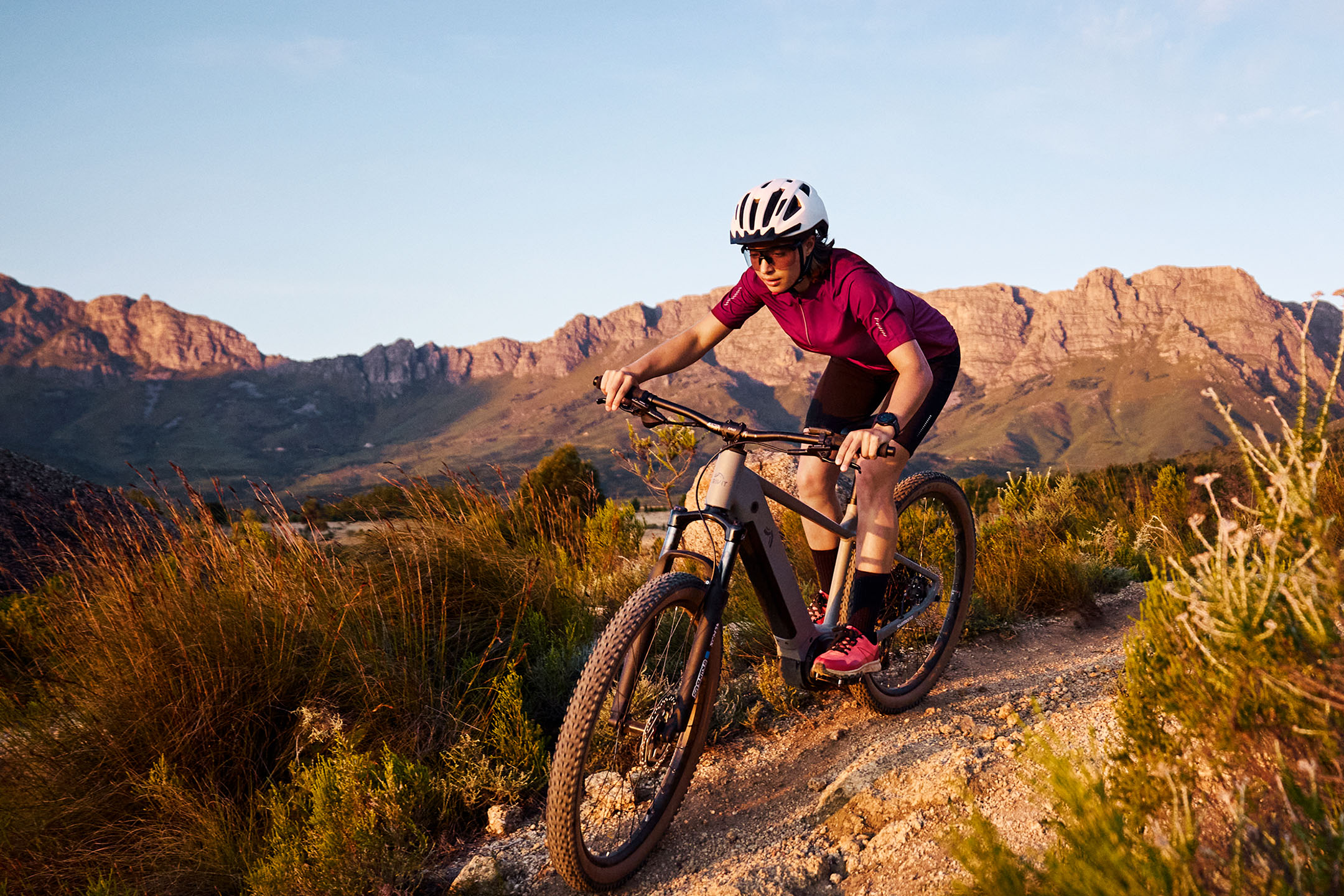 Žena na horském kole na polní cestě s horami v pozadí.