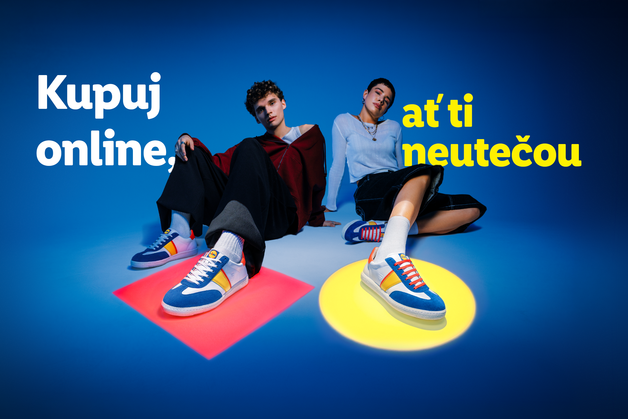 Dva mladí lidé sedí na zemi, na sobě mají barevné tenisky. Text: Kupuj online, ať ti neutečou.