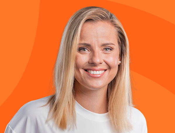 Žena s blond vlasy se usmívá na oranžovém pozadí.