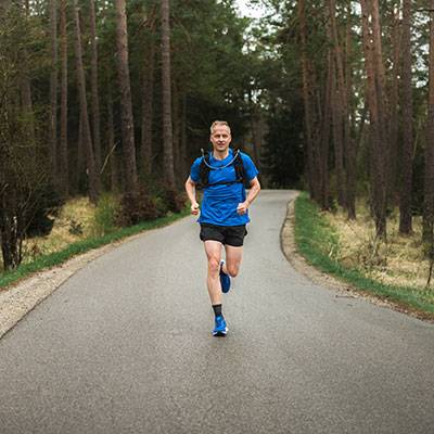 Muž běží v lese ve sportovním oblečení.
