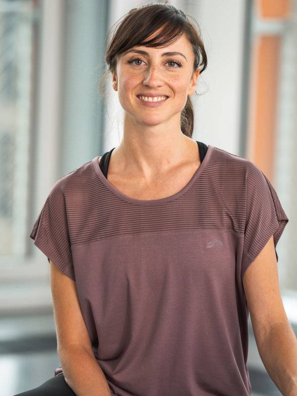 Usmívající se žena v krátkém fialovém sportovním topu.