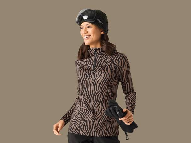 Žena v lyžařském topu se zebřím vzorem, černé čepici, brýlích a rukavicích.