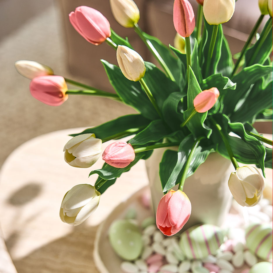 Váza růžových a bílých tulipánů s velikonočními vajíčky a sladkostmi na odkládacím stolku.