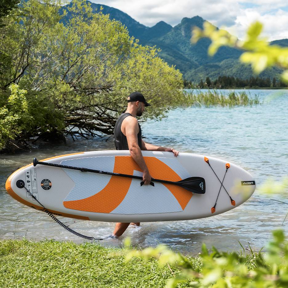 Muž s paddleboardem CRIVIT ve vodě, připravený pádlovat.