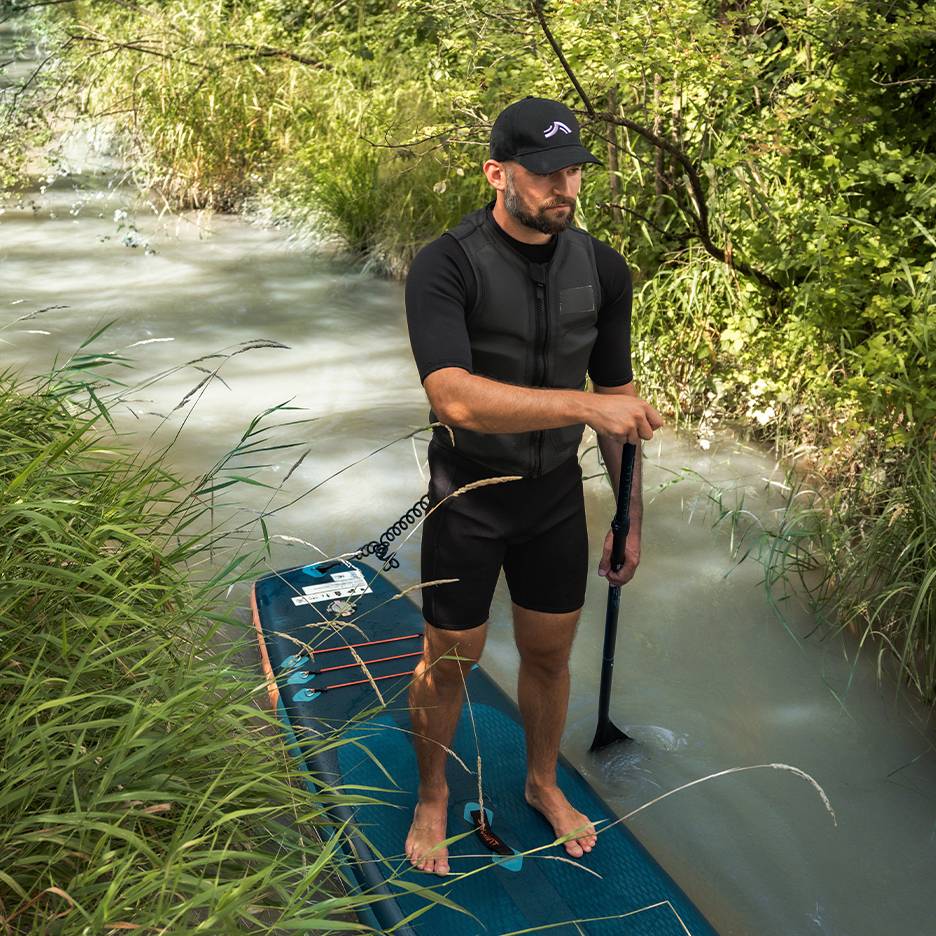 Muž na paddleboardu v řece, v neoprenu a záchranné vestě.