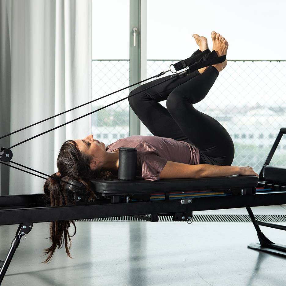 Žena cvičí nohy na pilates reformer stroji s odporovými pásy.