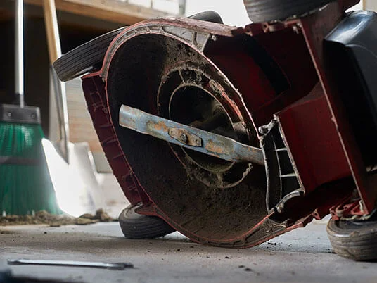 Špinavá sekačka na trávu vzhůru nohama, viditelná čepel