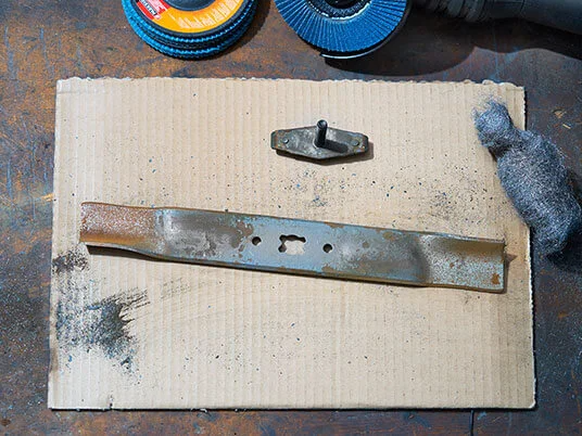 Zrezivělá čepel sekačky na kartonu s brusnými kotouči a ocelovou vlnou.