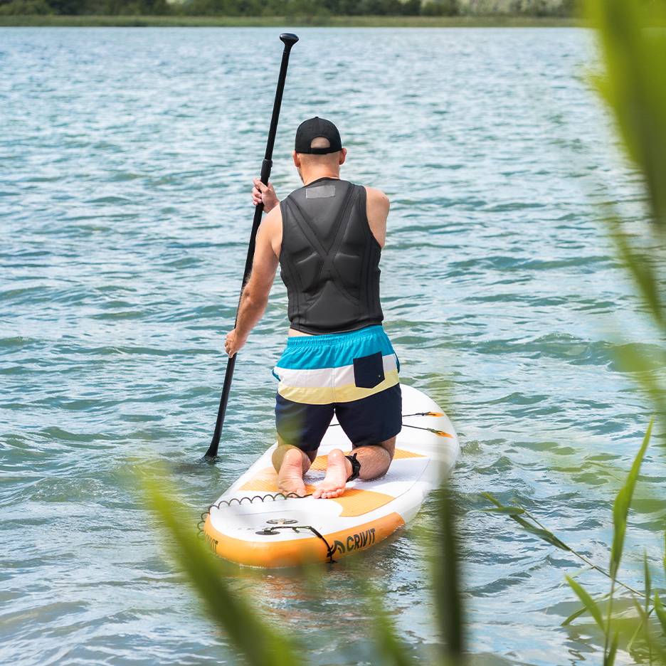 Muž pádluje na jezeře na SUP prkně Crivit, v záchranné vestě a plavkách.