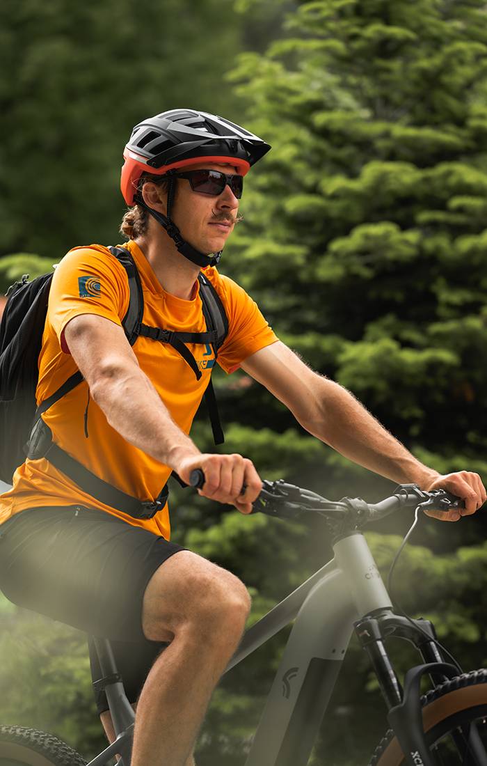 Cyklista v oranžovém tričku a helmě Giro jede na elektrokole Cube.