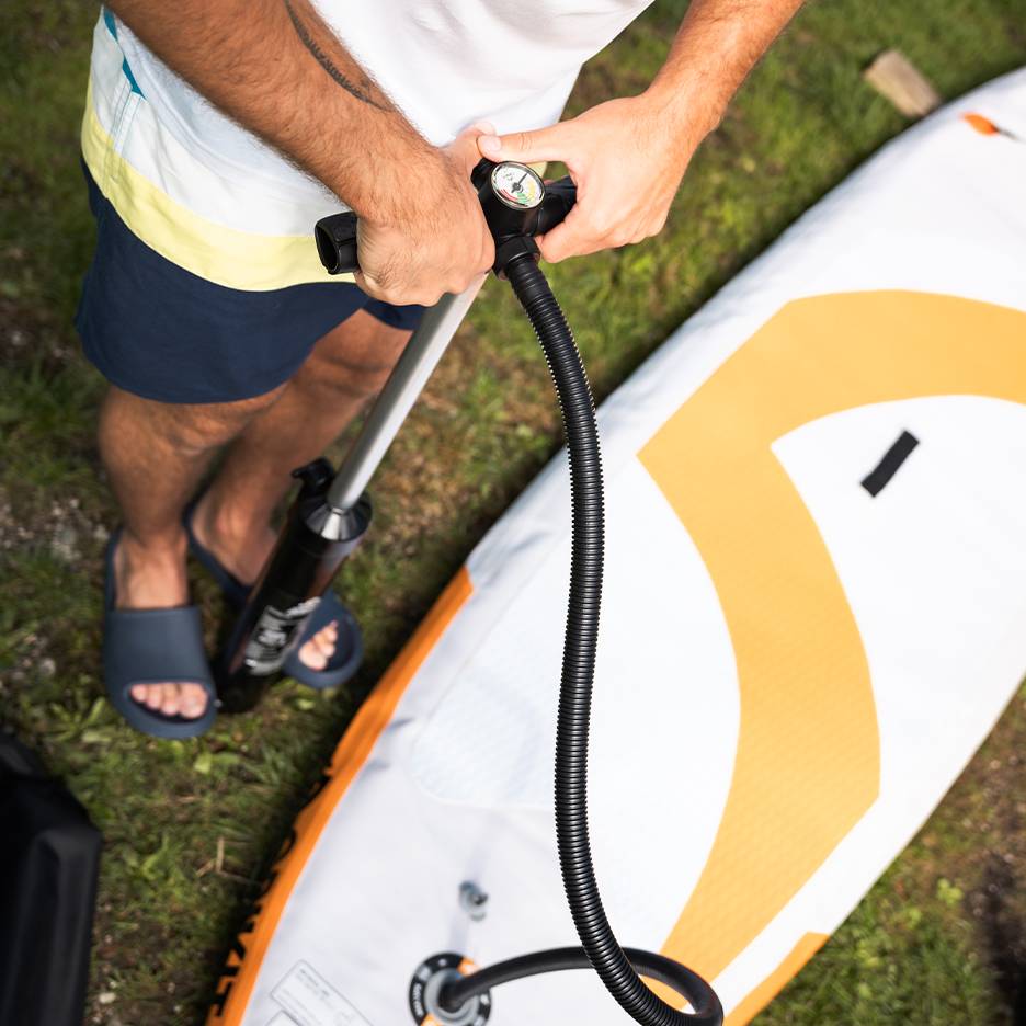 Muž nafukuje nafukovací paddleboard ruční pumpou.