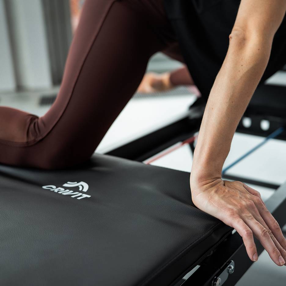 Žena cvičící na fitness stroji Crivit v hnědých jógových kalhotách.