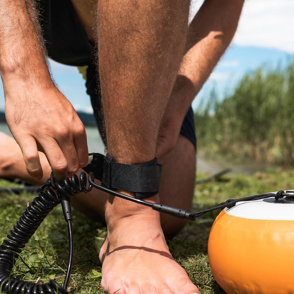 Muž si připíná vodítko na paddleboard k noze.