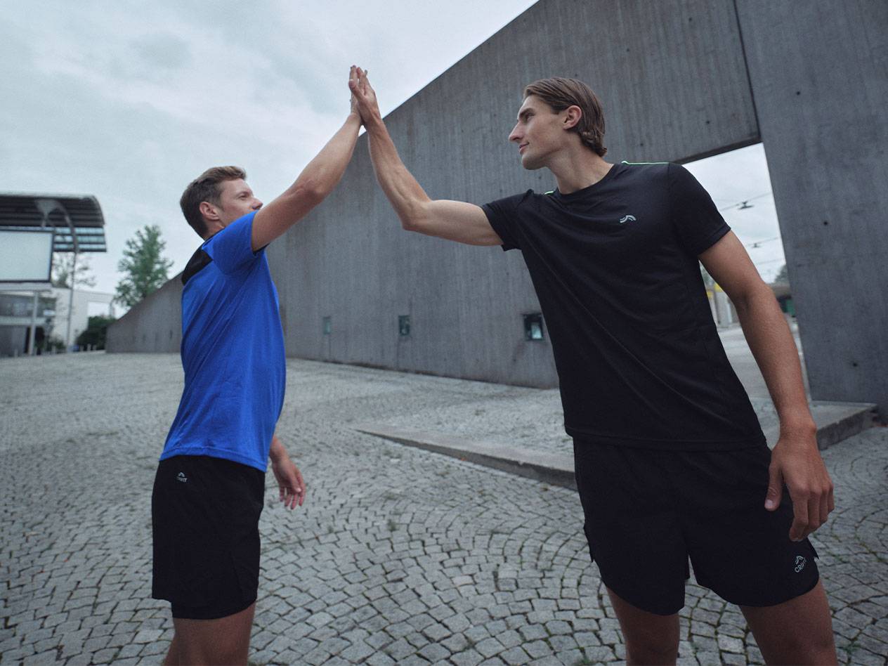 Dva muži v černých a modrých sportovních tričkách a šortkách si dávají high-five.
