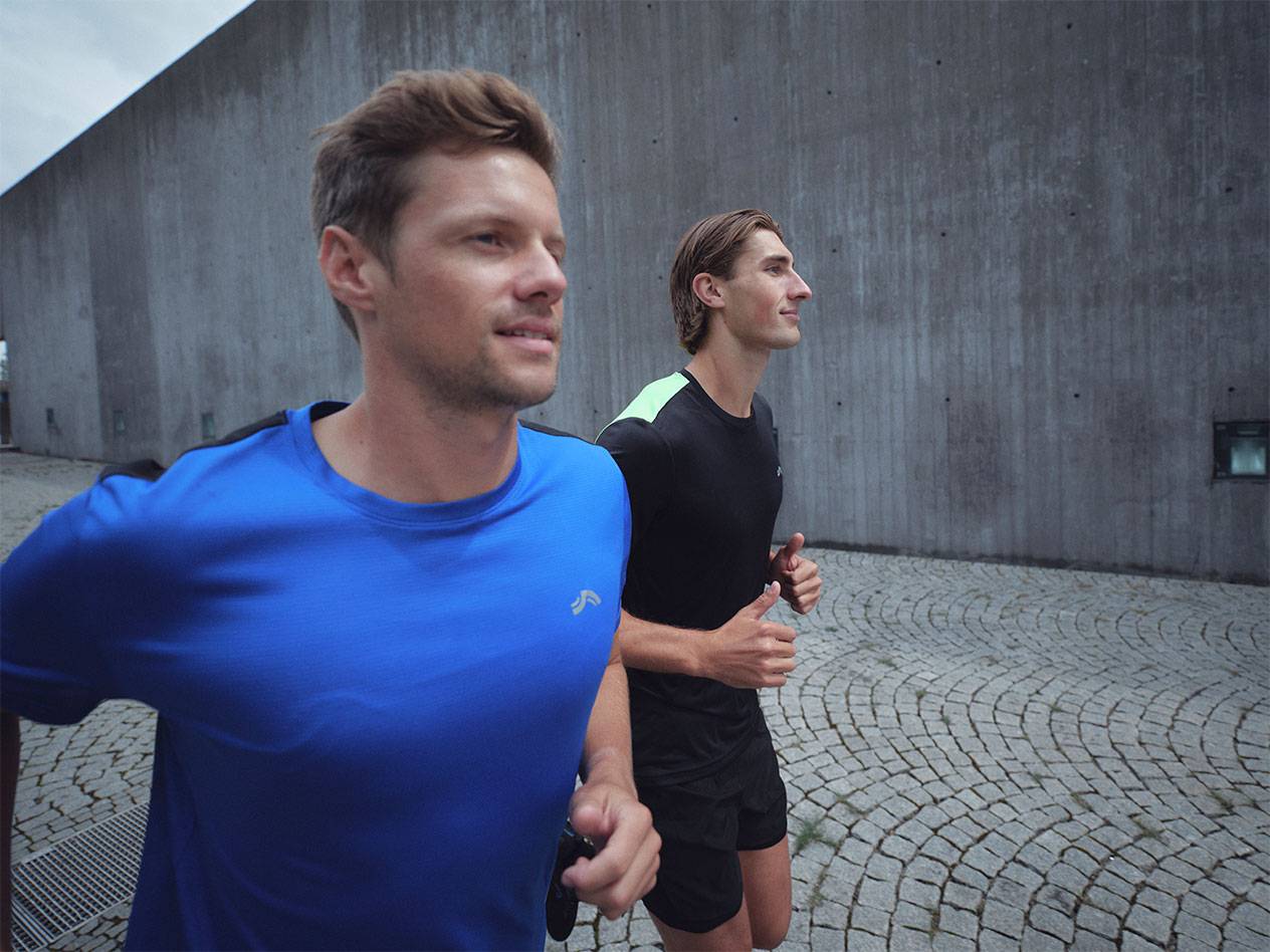 Dva muži běží ve sportovních tričkách a šortkách, jeden v modrém a jeden v černém.