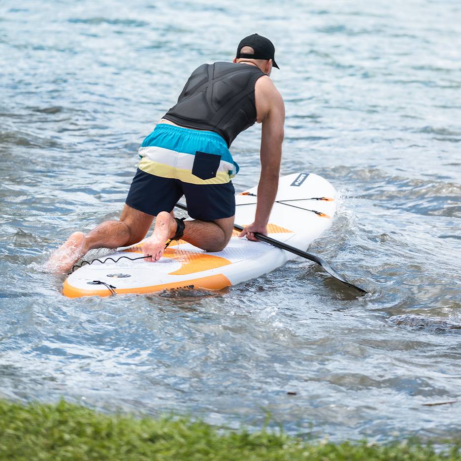 Muž klečící na paddleboardu s pádlem ve vodě.