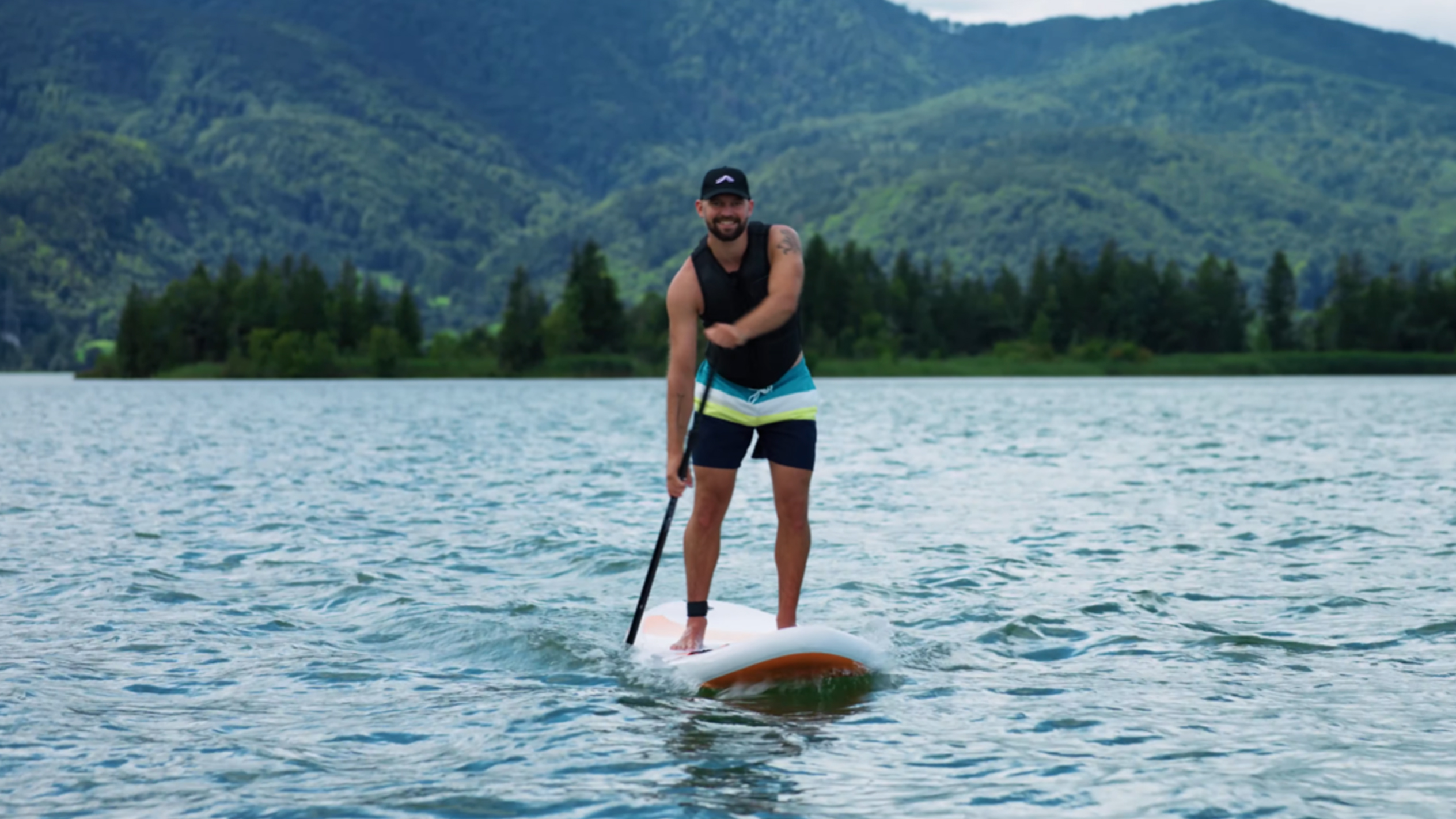 Muž na paddleboardu na jezeře s horami v pozadí.