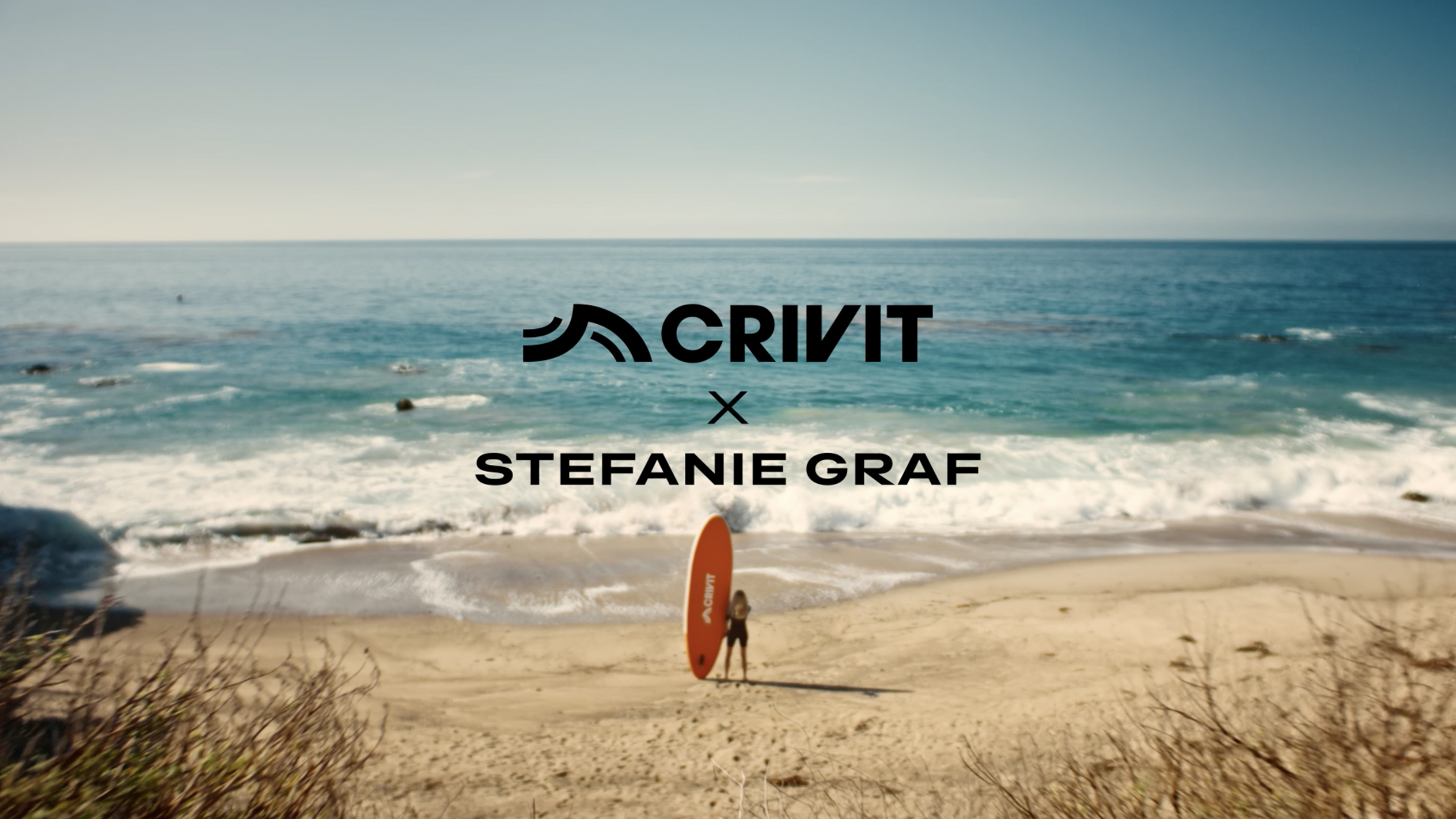 Žena s oranžovým SUP prknem na písečné pláži, s mořem v pozadí.